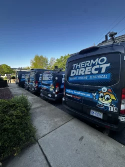 Four Thermo Direct service vans with company branding, specializing in mini-splits and central air cooling system solutions, are parked in a row along a sidewalk on a clear day.